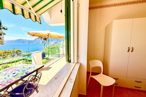 A balcony with a table, chairs, and an umbrella, overlooking a scenic view of a body of water and mountains.
