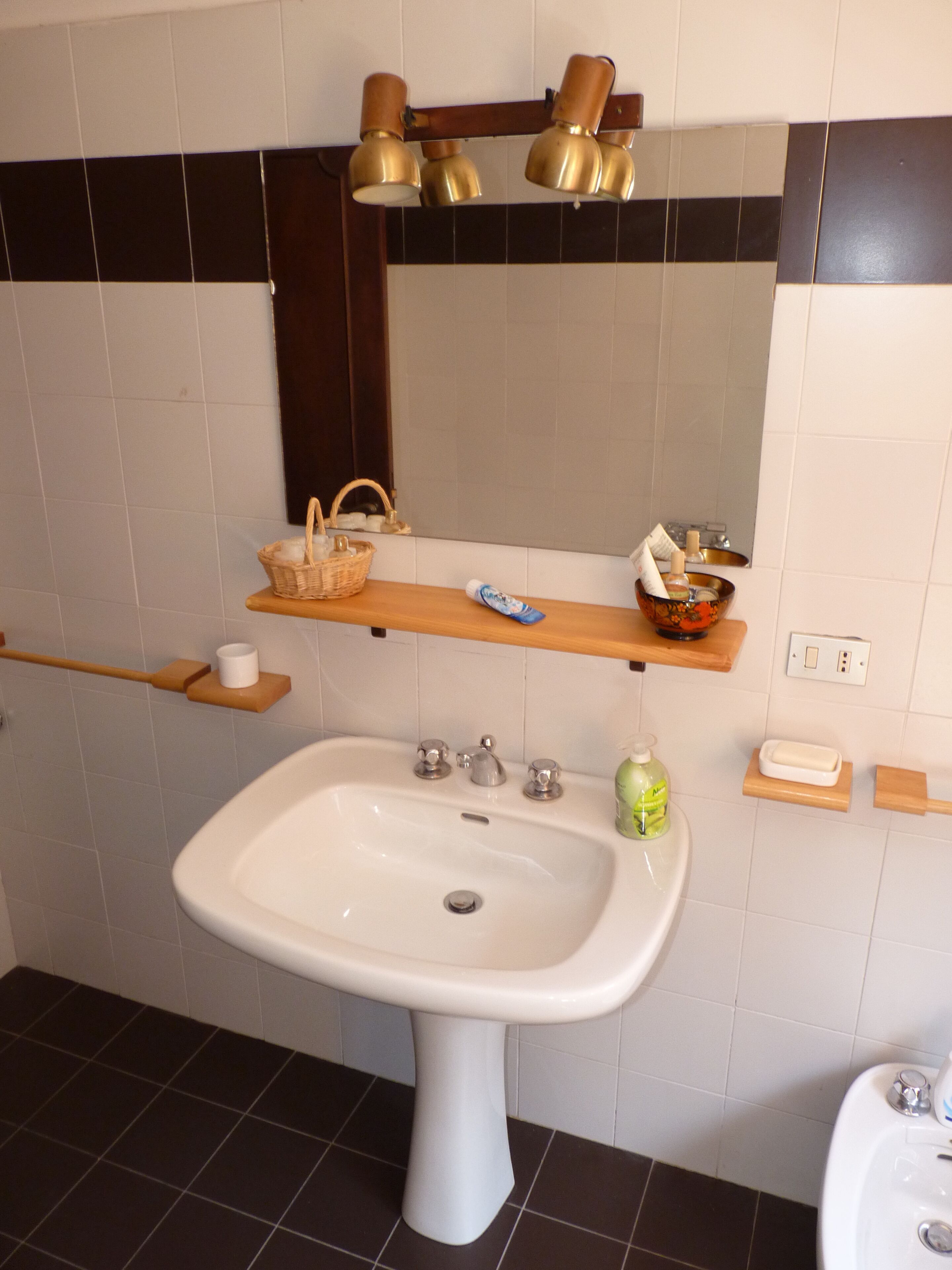 A bathroom with a white sink, a mirror, and a shelf with toiletries.