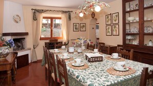 A dining room with a long table set for a meal, surrounded by chairs. There is a fireplace on the left, a window with curtains, and a cabinet with dishes on the right. - Villa degli Scoiattoli, 200-m² villa for 8-10 people with park and swimming pool (Casette D'ete, FM)