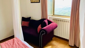 Een kamer met een paarse bank, een ingelijst kunstwerk aan de muur en een raam met uitzicht op het buitengebied.