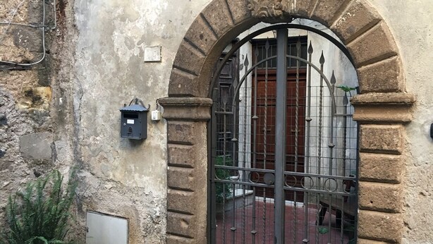 Een stenen gebouw met een metalen hekwerk, bloembakken en een geplaveid binnenhof.
