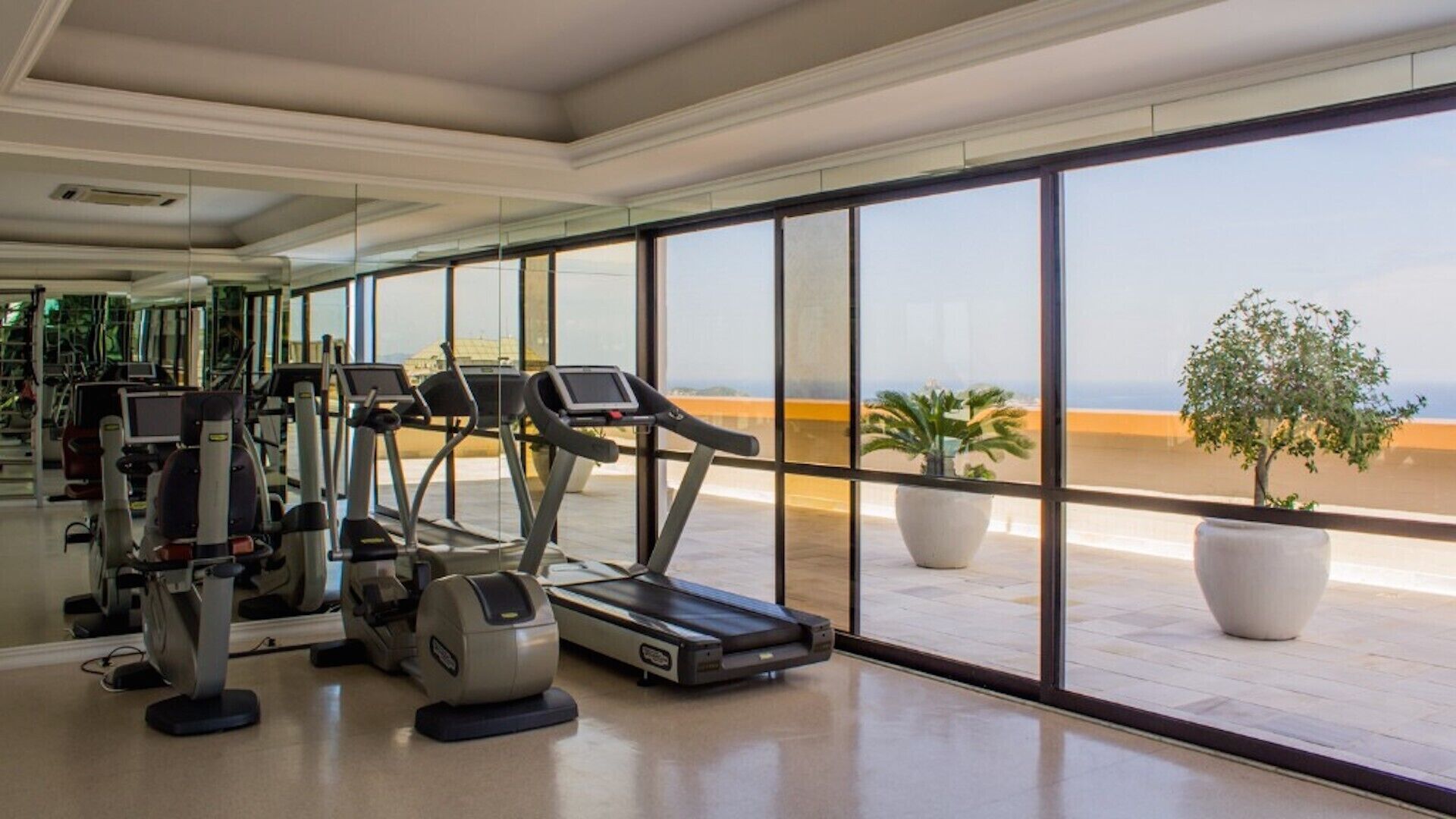 Une salle de sport équipée de tapis de course et d’appareils d’exercice, avec de grandes fenêtres donnant sur la plage.