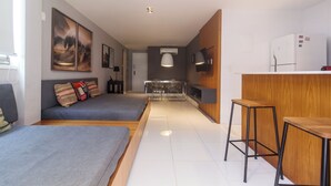 A modern, compact living space with a kitchenette, a dining area with bar stools, and a seating area with a sofa and pillows. - Barramares Ocean View (Rio de Janeiro)