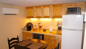 A compact kitchen with wooden cabinets, a white refrigerator, a microwave, and a small dining table with chairs. - Downtown Luxury Studio, Brevard NC (Brevard)