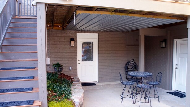 A covered patio with a table and chairs, a door, and a staircase leading to an upper level. - Downtown Luxury Studio, Brevard NC (Brevard)
