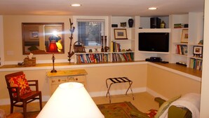 A living room with a bookshelf, a television, a lamp, and a window. - Downtown Luxury Studio, Brevard NC (Brevard)