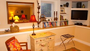 A cozy living room with a wooden cabinet, a red lamp, a bookshelf, a television, and a window with blinds. - Downtown Luxury Studio, Brevard NC (Brevard)