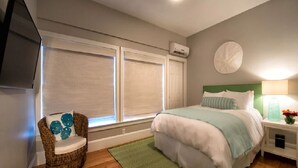 A bedroom with a bed, a chair, a nightstand, a lamp, and a wall-mounted TV. - Two Level Condo with all the Essentials, Thames St (Newport)