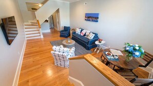 A modern living room with a wooden staircase, a blue sofa set, and a dining area with a wooden table and chairs. - Two Level Condo with all the Essentials, Thames St (Newport)