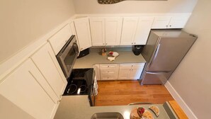 A compact kitchen with white cabinets, a stainless steel refrigerator, a stove, and a sink. - Two Level Condo with all the Essentials, Thames St (Newport)