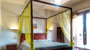 Un lit à baldaquin, une table de chevet, une petite table et une lampe fixée au mur.