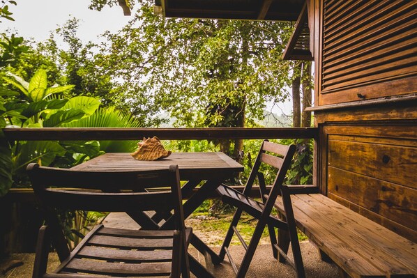 Una terraza de madera con una mesa y sillas, rodeada de abundante vegetación.