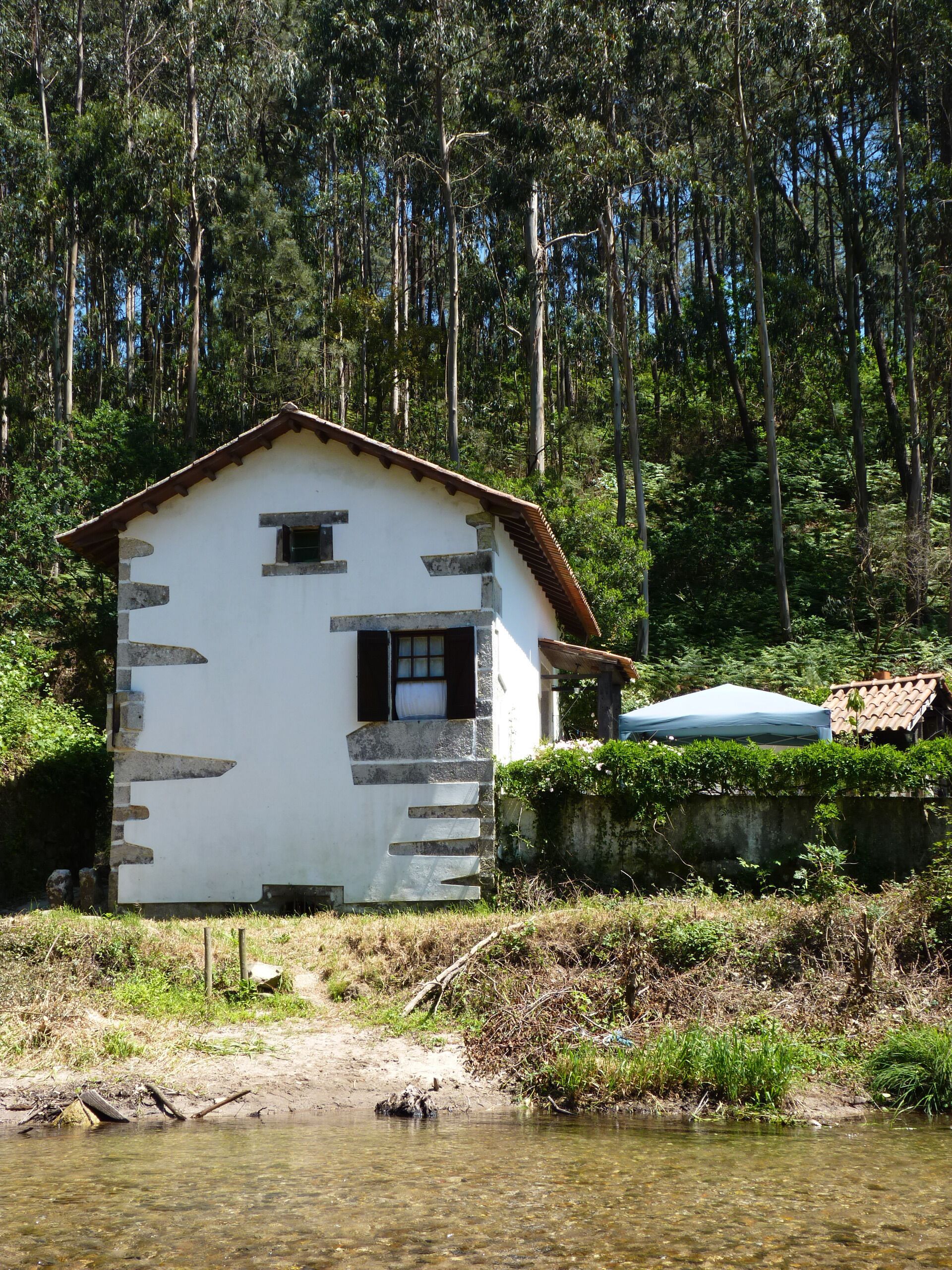 Una casa de piedra rústica con techo inclinado, ubicada junto a un arroyo cristalino.