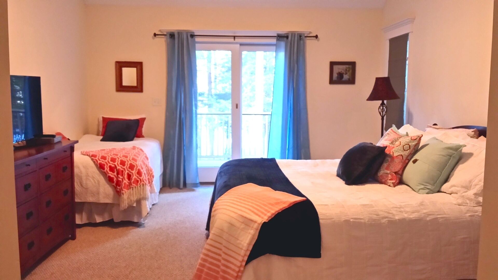 A hotel room with two beds, a TV, a dresser, and a window with curtains.