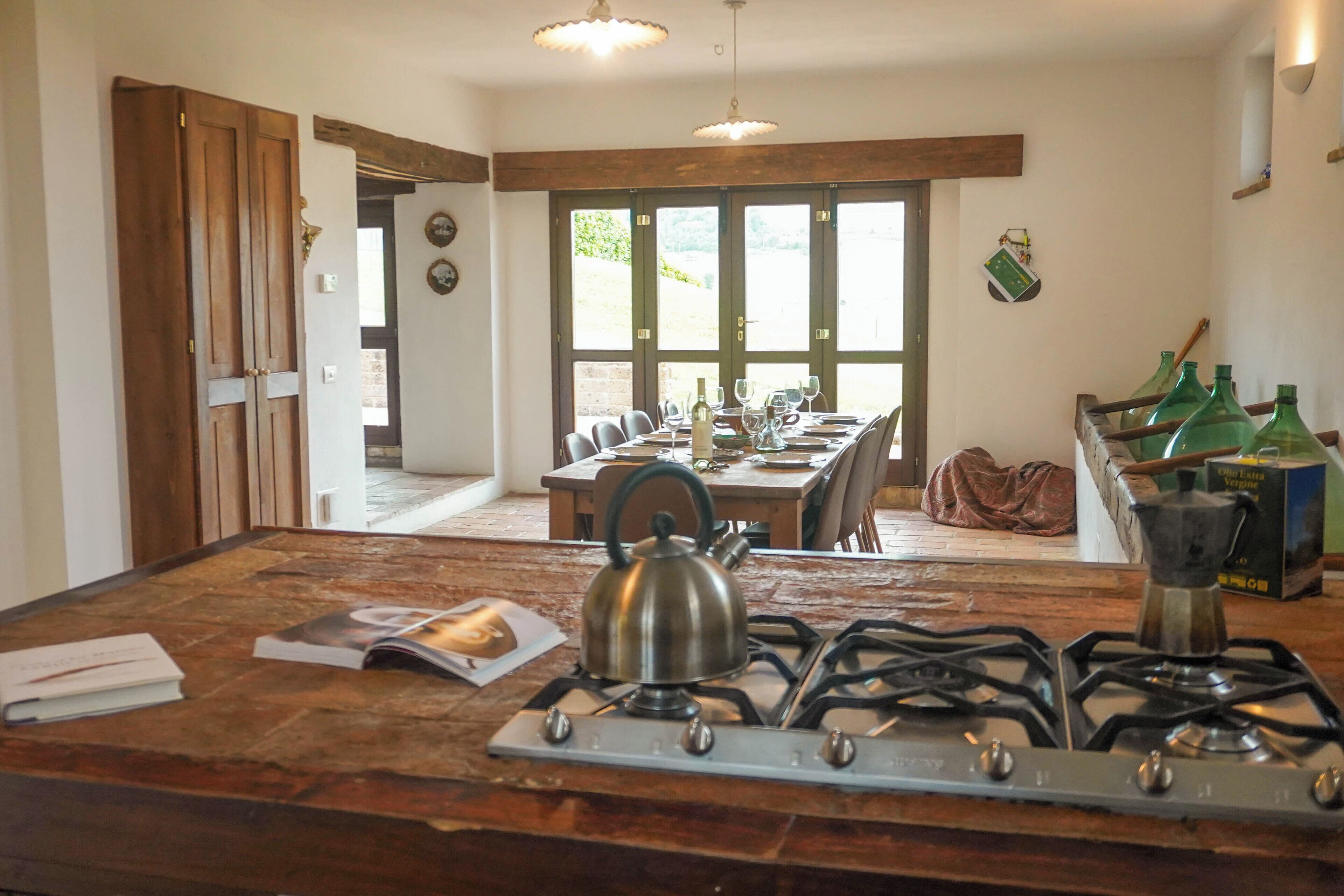 A kitchen with a gas stove, kettle, and a dining table set for six.