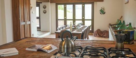 A kitchen with a gas stove, kettle, and a dining table set for six.
