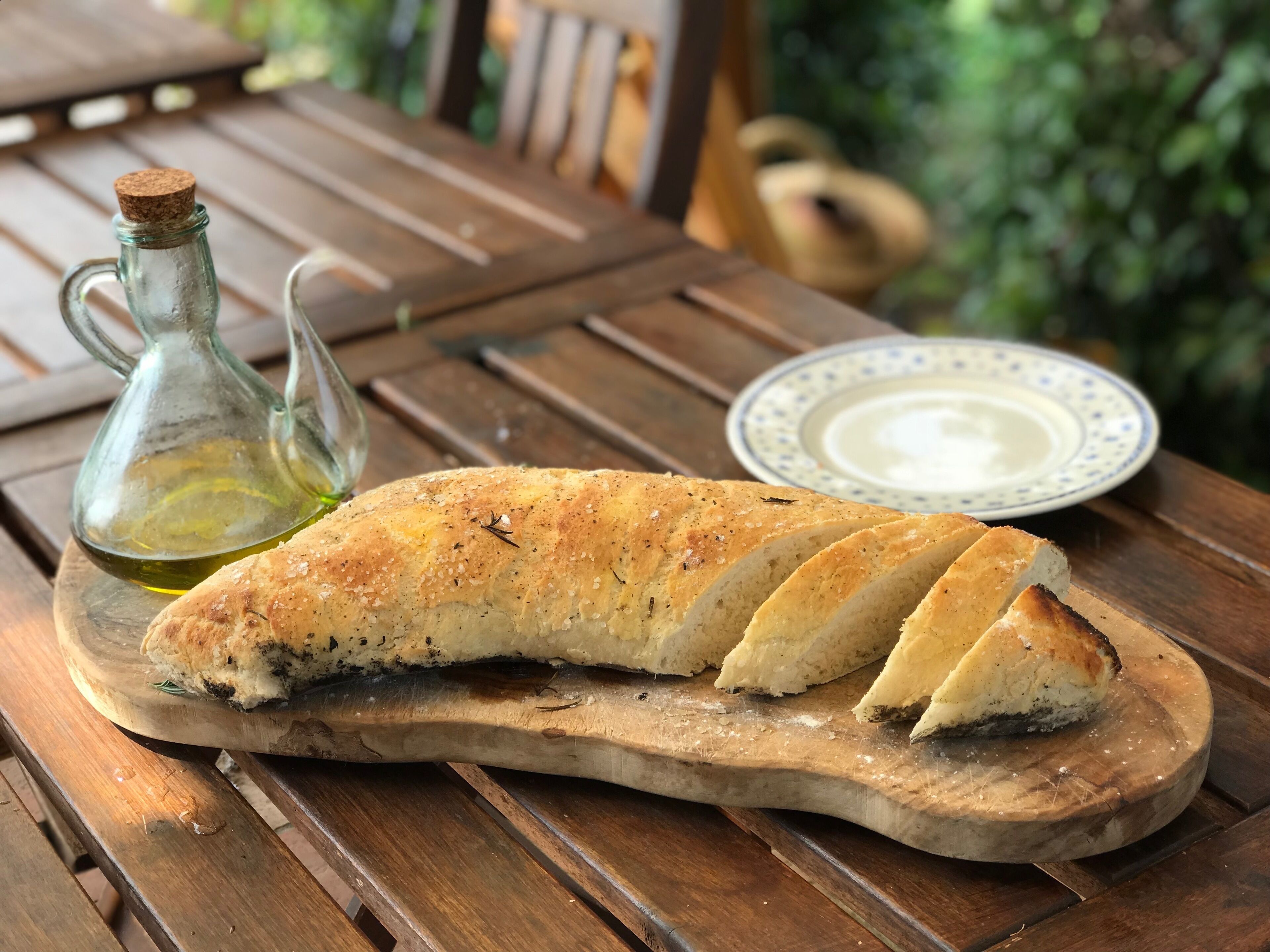Une miche de pain sur une planche à découper en bois, avec une bouteille d’huile et une assiette de beurre.