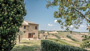A rustic stone house with a tiled roof, surrounded by lush greenery and rolling hills.
