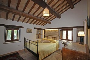 Ein Schlafzimmer mit Bett, Nachttisch, Lampe, Fenster und einer Steinwand.