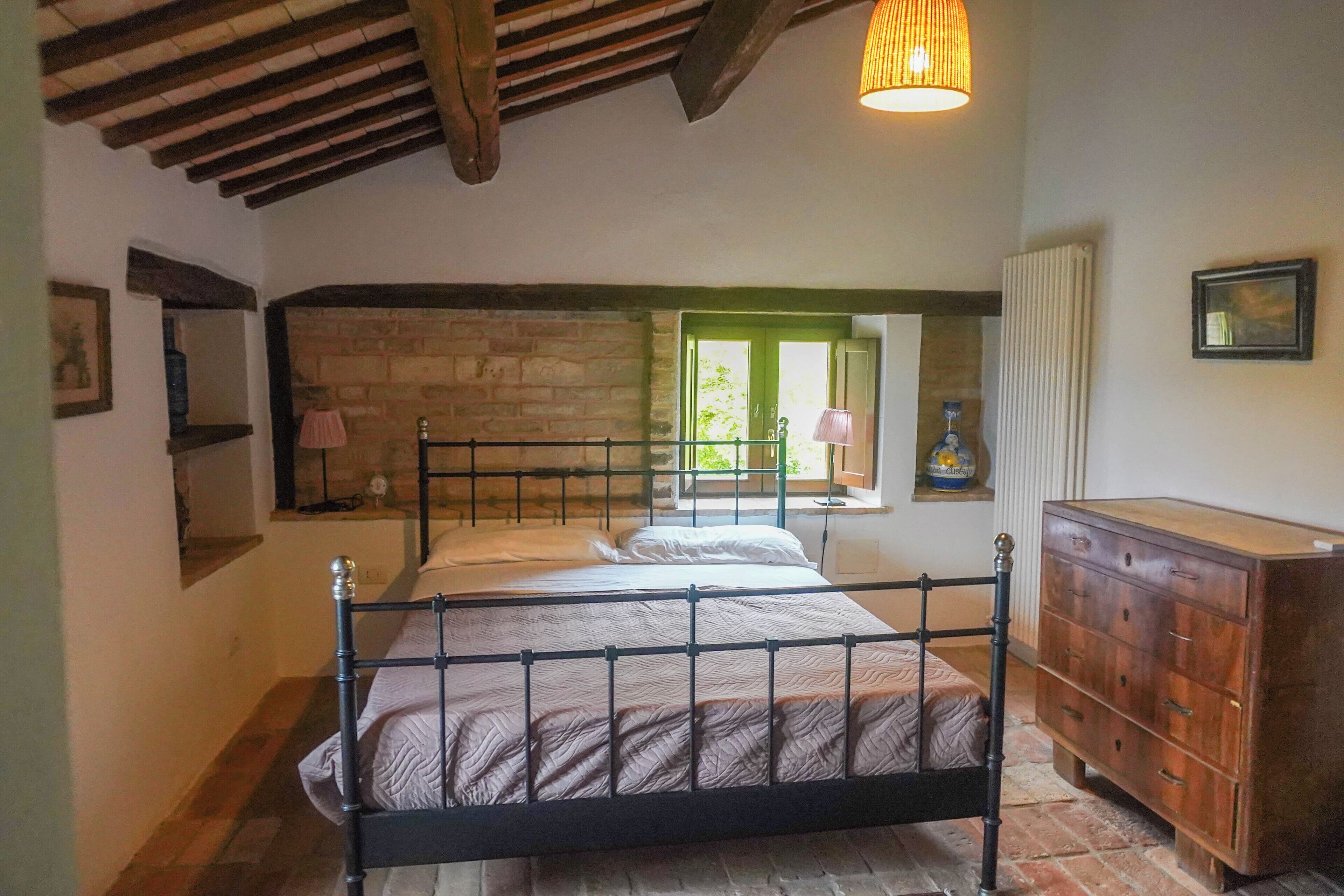 Un dormitorio con pared de piedra, techo de madera, cama, cómoda y ventana con vistas.