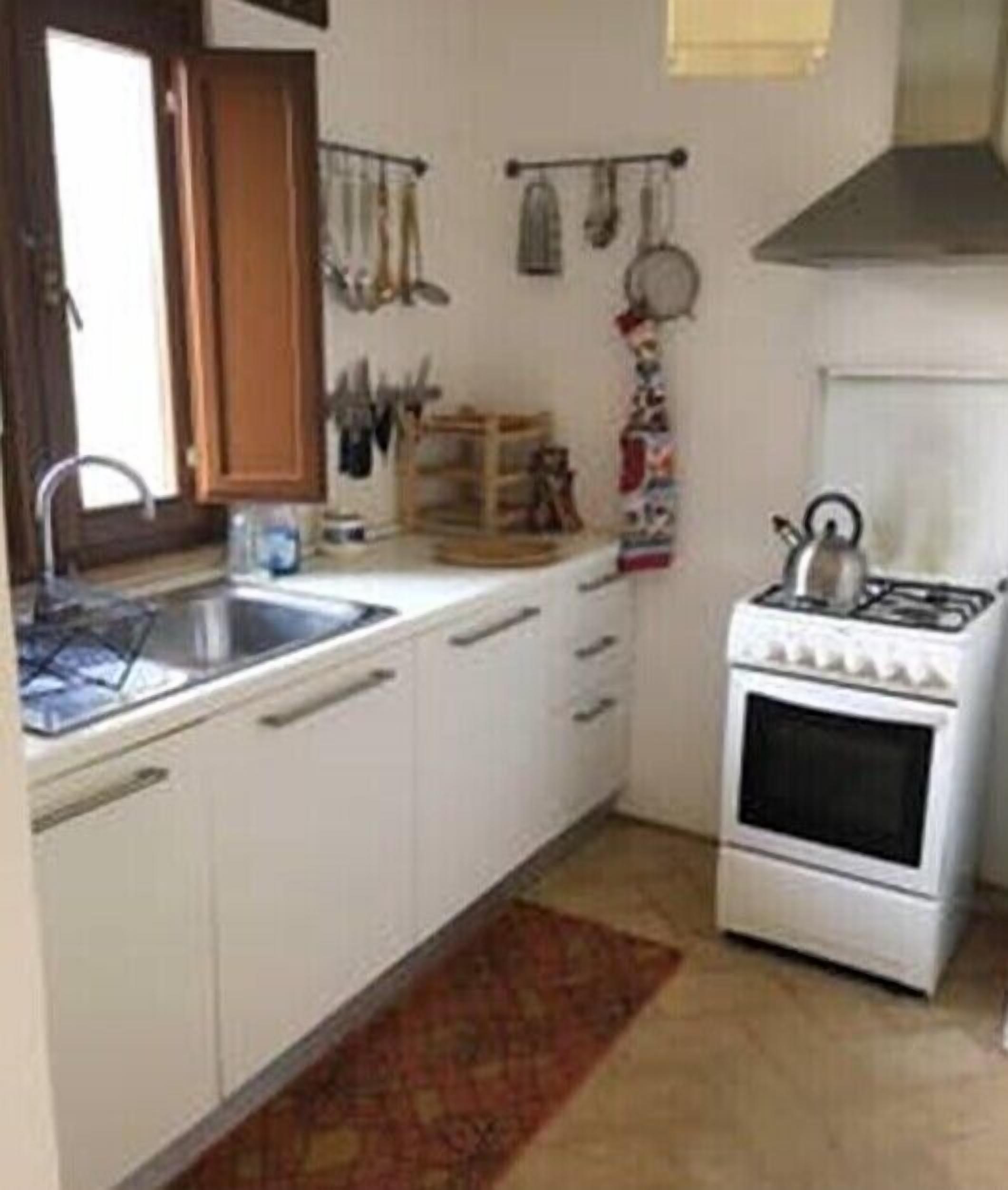 A small kitchen with white cabinets, a gas stove, a sink, and hanging utensils.