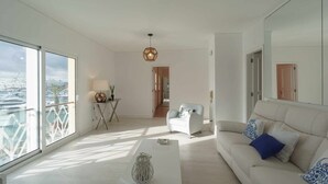 A modern living room with a white sofa, a coffee table, and a view of a marina through large windows.