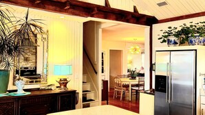 Een keuken met een groot eiland, houten barstoelen, een roestvrijstalen koelkast en een trap naar een andere kamer.