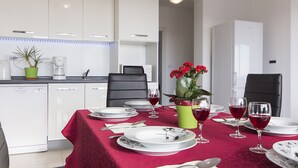 Un coin repas avec une nappe rouge, des assiettes blanches et des verres à vin rouge. On y trouve deux chaises, une plante en pot et un vase avec des fleurs rouges.