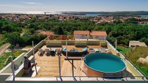 Un espace piscine aménagé sur le toit, offrant une vue sur une ville côtière, et comprenant une piscine et des chaises longues.