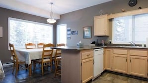 A kitchen with wooden cabinets, a dishwasher, and a dining area with a table and chairs. - Fabulous Four Bedroom Home - Ski in/Ski Out - 3-Minute Flat Walk to the Village (Silver Star Mountain)