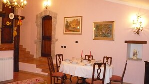 Un comedor con una mesa dispuesta para cuatro personas, sillas de madera, una araña y dos cuadros en la pared.