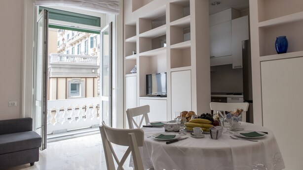 Un comedor con una mesa preparada para dos, un balcón con barandilla blanca y vistas a un edificio.