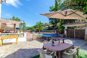 Une terrasse extérieure équipée d’une table de ping-pong, d’un baby-foot et d’une table à manger pour deux personnes.
