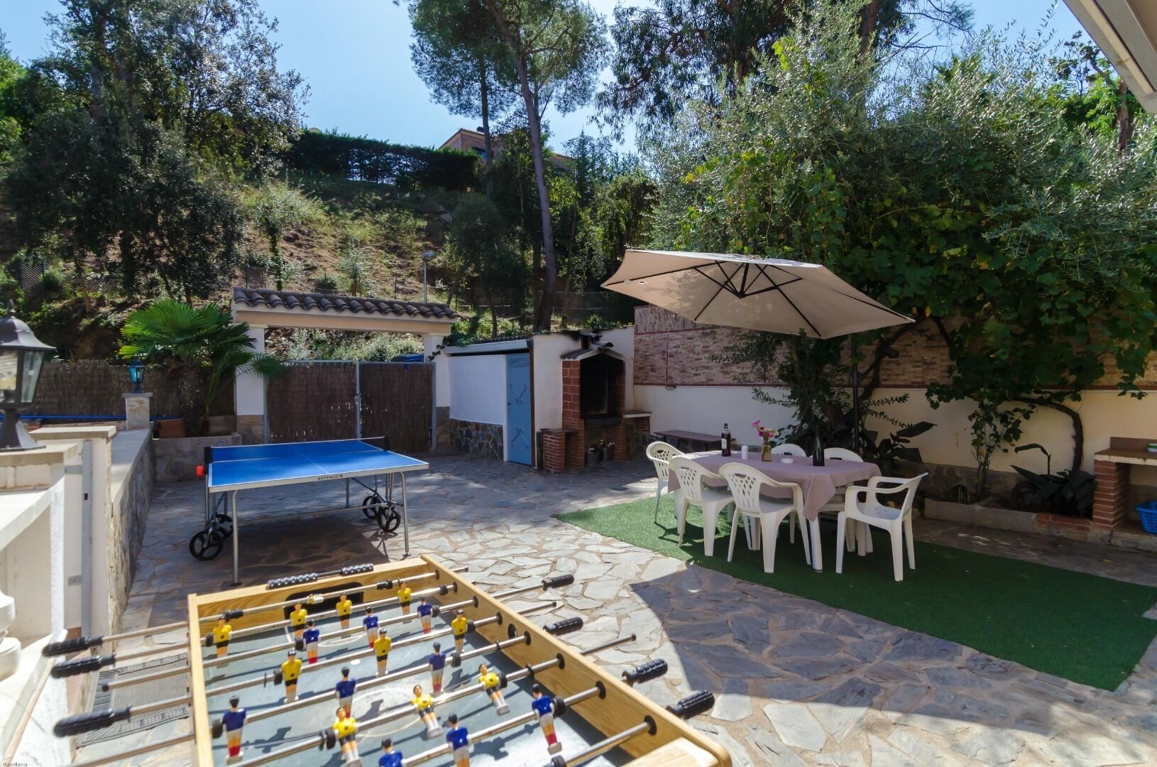 Un patio con mesa de futbolín, mesa de comedor con sillas y una sombrilla.