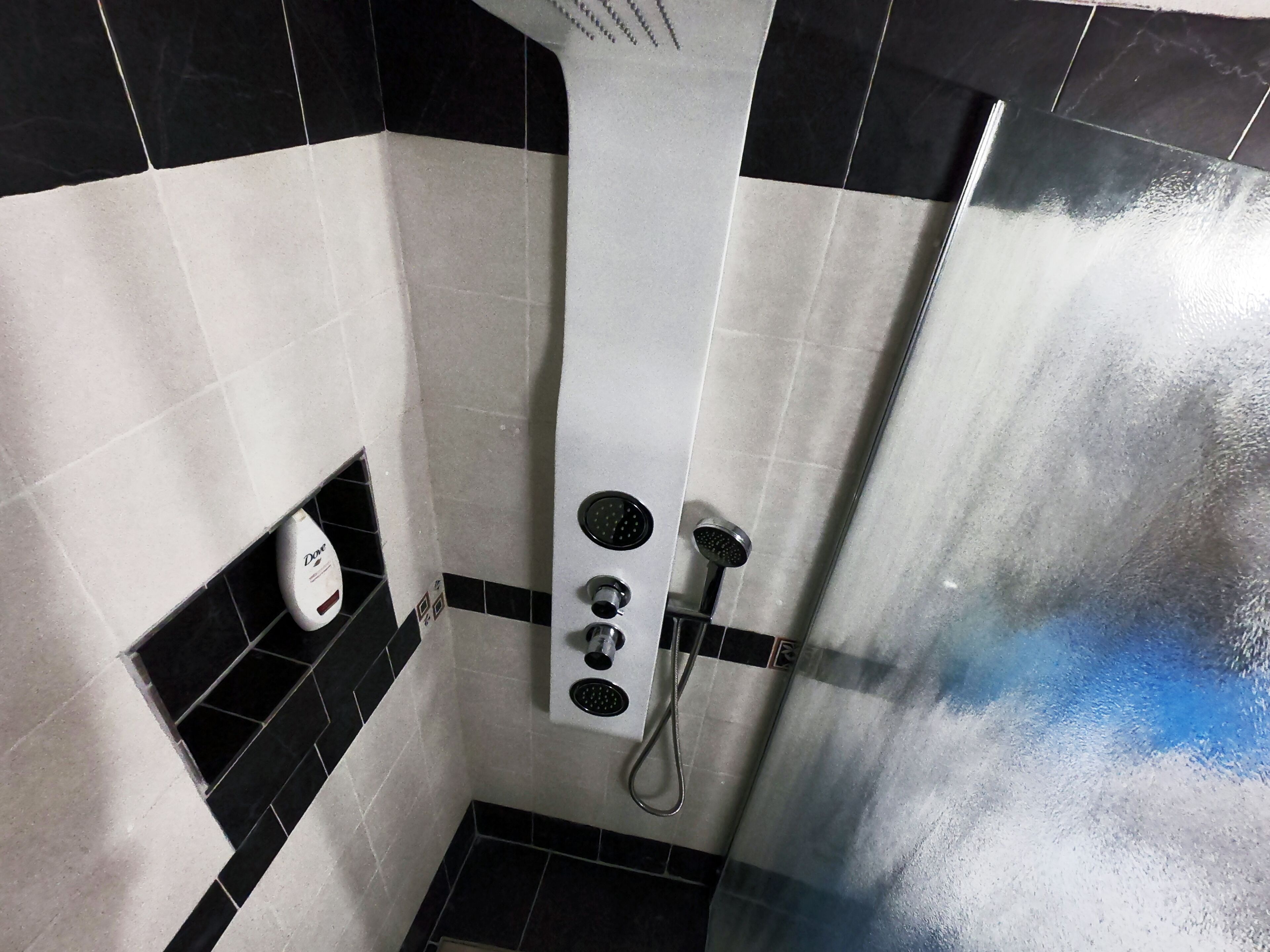 A bathroom with black and white tiles, a shower with a handheld showerhead, and a soap dispenser.