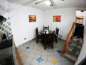 A dining area with a round table and chairs, a tiled floor with a geometric pattern, and two wall-mounted paintings. - Independent apartment with sea view terrace in the historic center of Lipari (Lipari)