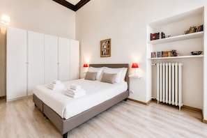 A bedroom with a bed, bedside lamps, a radiator, a wardrobe, and a bookshelf.