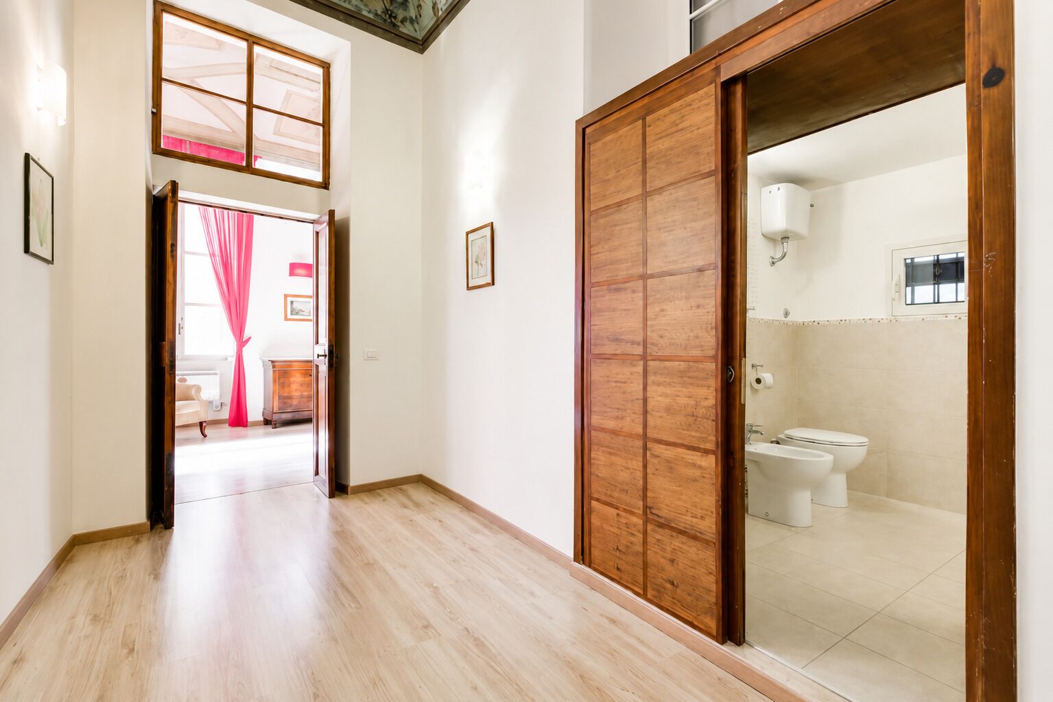 Un pasillo con piso de madera que lleva a una habitación con inodoro y bañera.