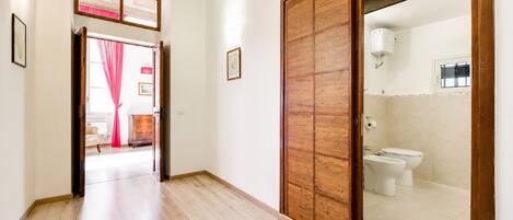Un pasillo con piso de madera que lleva a una habitación con inodoro y bañera.