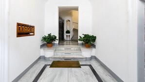 Un corridoio con pavimento in marmo, una slitta portacenere in legno e due piante in vaso.