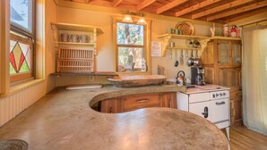 Une cuisine rustique avec des poutres en bois, un grand évier en pierre et des appareils électroménagers d’époque.