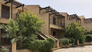 A building with a stone-paved courtyard, balconies with metal railings, and surrounding greenery. - Villa 200 mt. from the sea (San Vito Lo Capo)