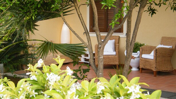 A patio area with wicker furniture, a white planter, and lush greenery. - Villa 200 mt. from the sea (San Vito Lo Capo)
