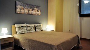 A neatly made bed with a quilted bedspread, two bedside lamps, and a wall-mounted TV. - Villa 200 mt. from the sea (San Vito Lo Capo)