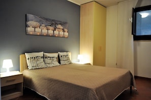A neatly made bed with a quilted bedspread, two bedside lamps, and a wall-mounted TV.