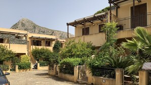 A stone-paved street in a residential area with buildings, a mountain in the background, and some greenery. - Villa 200 mt. from the sea (San Vito Lo Capo)