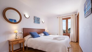 A bedroom with a wooden headboard, two beds with white bedding, a bedside table with a lamp, a round mirror, and a view of the outdoors through a window with curtains. - FINCA MARINA  VT/121 ref. VP11 (Pollensa / Pollença)