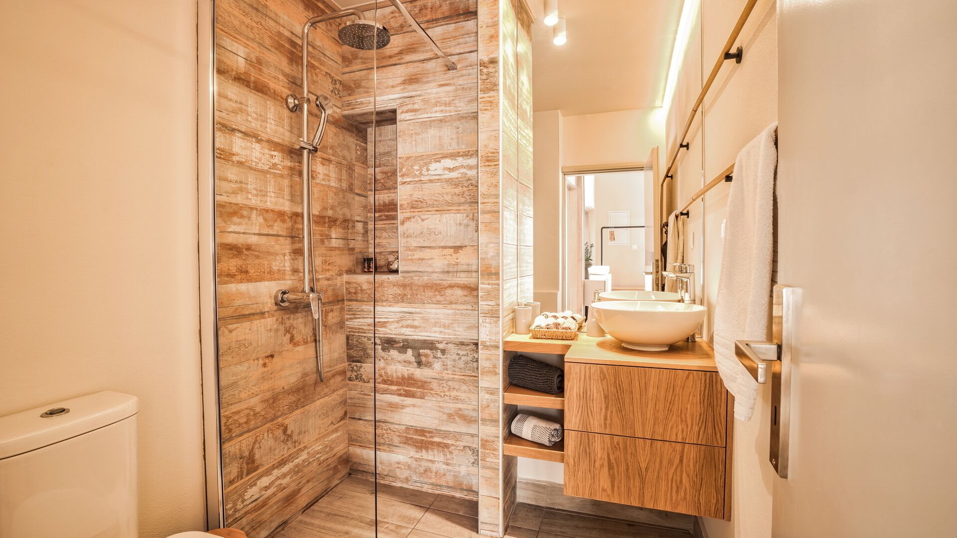 Een moderne badkamer met een douche met glazen wand, houten wandbekleding, een houten wastafelmeubel met een wastafel en een spiegel.