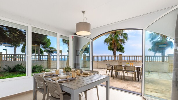 A modern outdoor dining area with a table and chairs, large windows, and a view of the sea. - Beachfront apartment perfect for families - UHC GLADIOLS 211 (Cambrils)