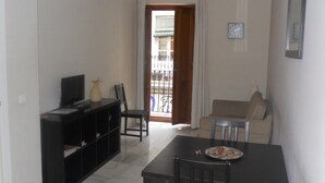 Een compacte, moderne woonkamer met een eettafel, stoelen, een televisie en een boekenkast.